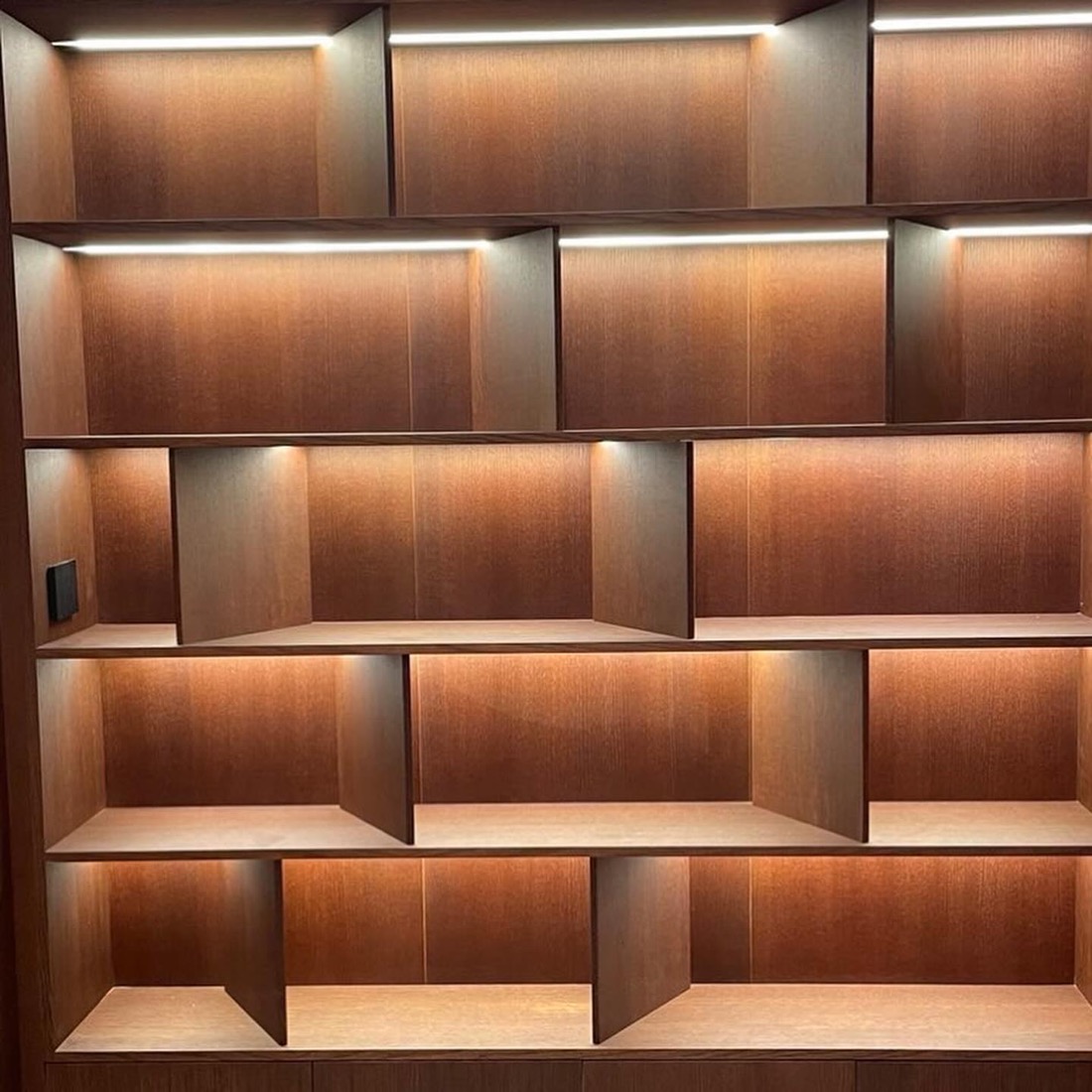 Bibliotekë muri prej druri me ndriçim të integruar në secilën nishë